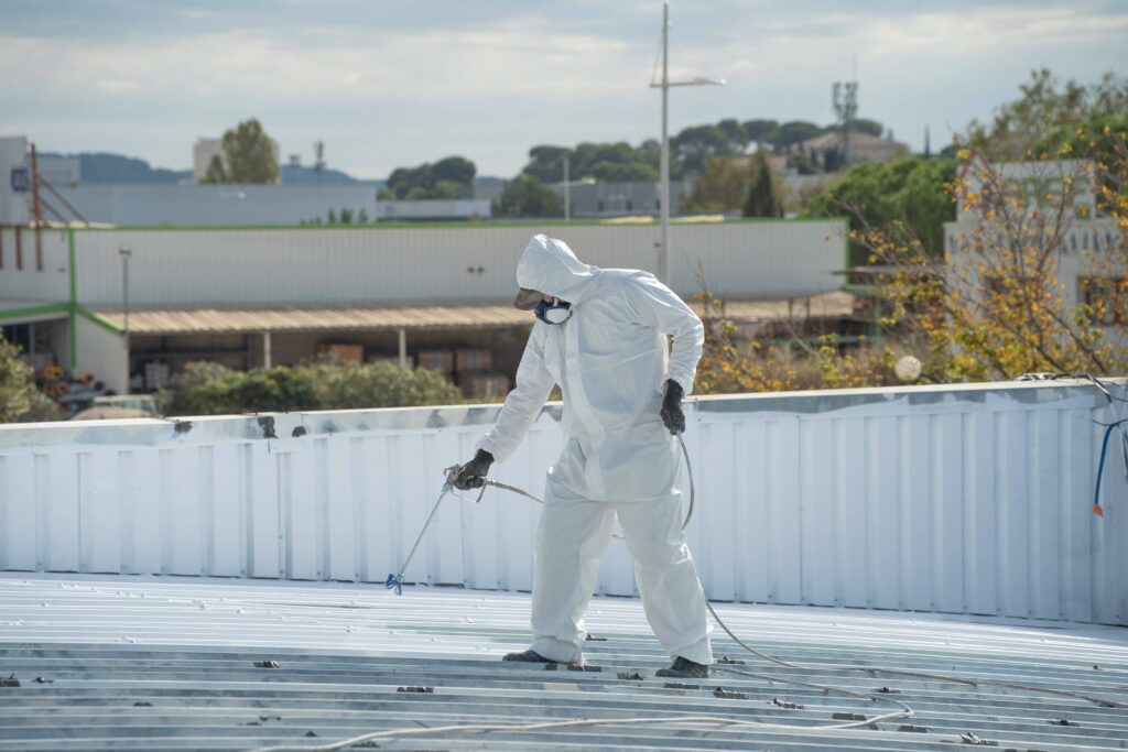 Un applicateur en équipement de protection appliquant une résine de cool roofing sur une toiture industrielle, démonstration de la mise en œuvre d'une toiture froide.